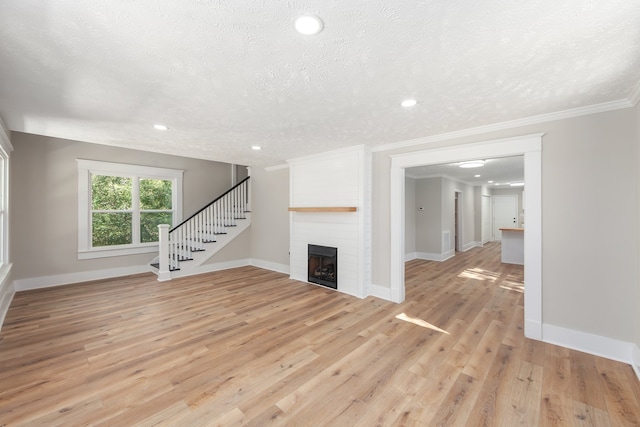 unfurnished living room with a large fireplace, a textured ceiling, light hardwood / wood-style flooring, and ornamental molding