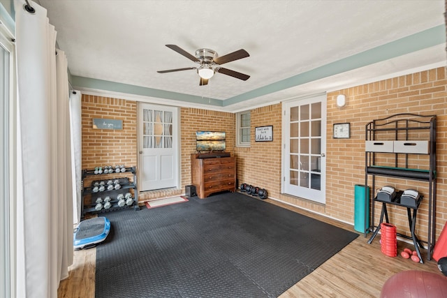 workout area featuring ceiling fan, brick wall, and wood-type flooring