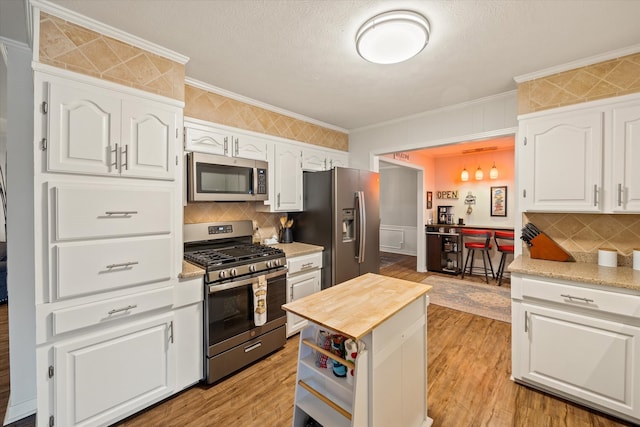 kitchen with white cabinetry, stainless steel appliances, ornamental molding, and light hardwood / wood-style flooring