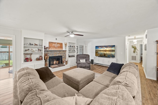 living room with a stone fireplace, ornamental molding, built in features, light wood-type flooring, and ceiling fan