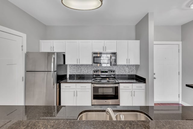 kitchen featuring dark stone countertops, white cabinetry, stainless steel appliances, and tasteful backsplash