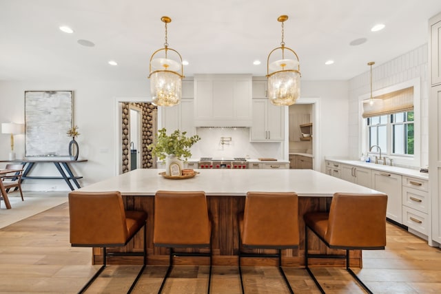 kitchen with a large island, a notable chandelier, light wood-type flooring, and custom exhaust hood