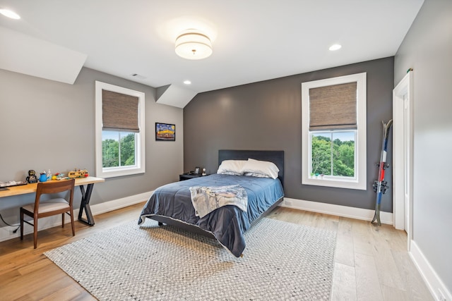 bedroom with vaulted ceiling, multiple windows, and light hardwood / wood-style floors