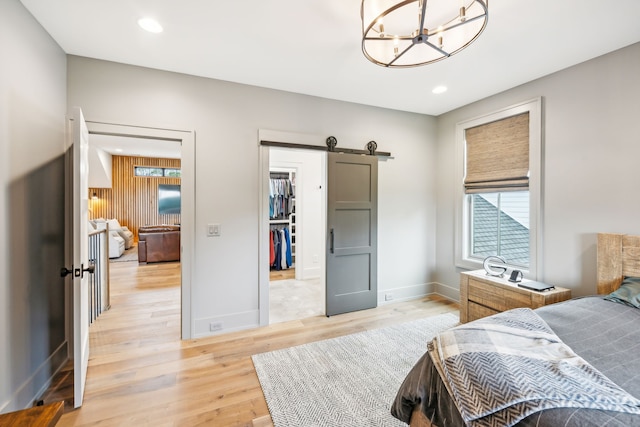 bedroom with a barn door, a spacious closet, a closet, light hardwood / wood-style floors, and a notable chandelier