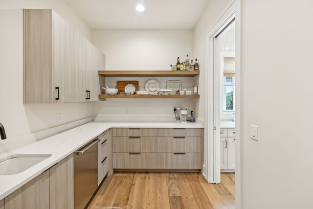 bar with light stone countertops, stainless steel dishwasher, light brown cabinetry, light hardwood / wood-style floors, and sink