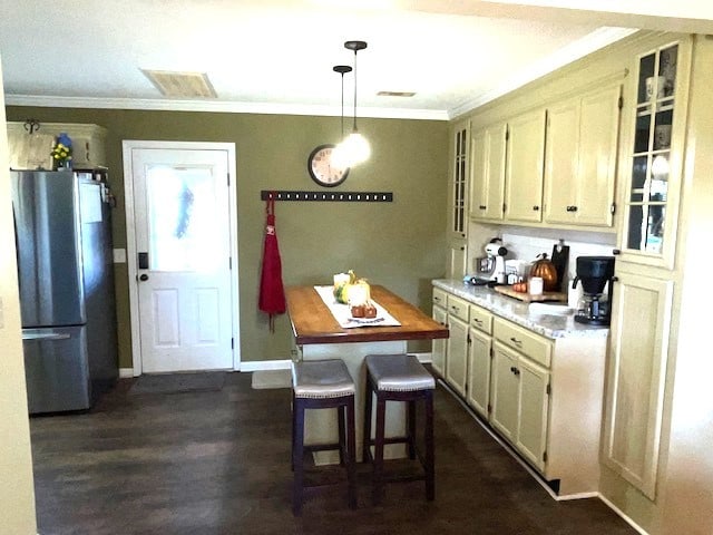 kitchen with crown molding, decorative light fixtures, stainless steel refrigerator, dark hardwood / wood-style floors, and a kitchen breakfast bar