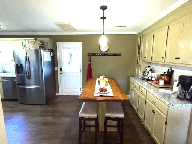 kitchen with light stone counters, ornamental molding, appliances with stainless steel finishes, decorative light fixtures, and dark hardwood / wood-style flooring