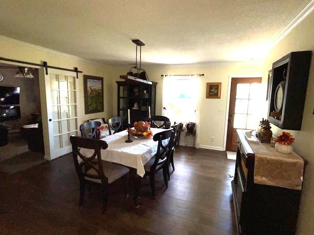 dining area with a barn door, a textured ceiling, dark hardwood / wood-style flooring, and ornamental molding