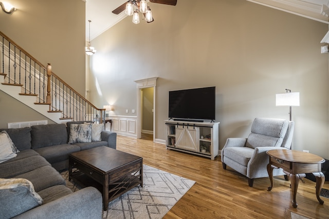 living room with wainscoting, a towering ceiling, ornamental molding, wood finished floors, and stairs