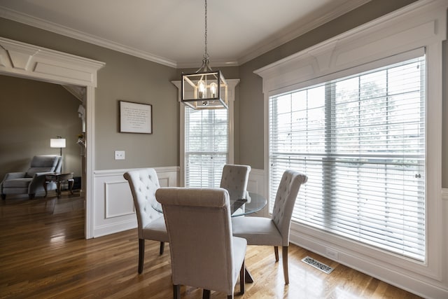 dining space featuring crown molding, dark wood finished floors, a notable chandelier, visible vents, and wainscoting