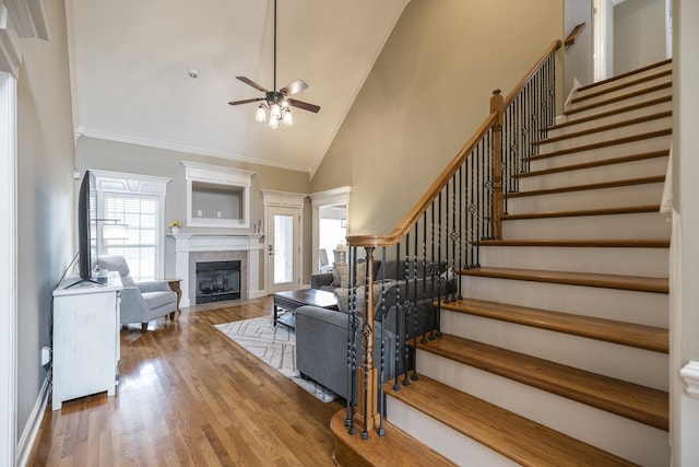 living room with a fireplace with flush hearth, stairway, ornamental molding, wood finished floors, and high vaulted ceiling