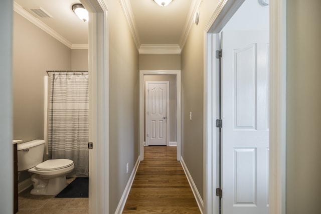 hallway featuring baseboards, visible vents, wood finished floors, and ornamental molding