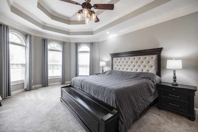 bedroom with ceiling fan, light colored carpet, baseboards, ornamental molding, and a tray ceiling