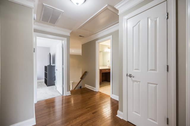 hall featuring dark wood-type flooring, visible vents, an upstairs landing, ornamental molding, and attic access