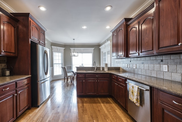 kitchen featuring crown molding, light wood finished floors, stainless steel appliances, tasteful backsplash, and a sink