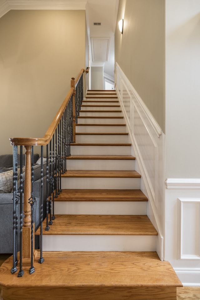 stairway with attic access, visible vents, and crown molding