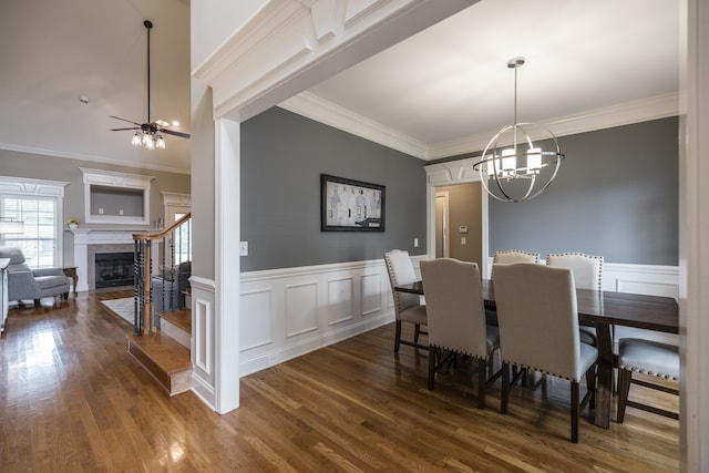 dining space with a wainscoted wall, a fireplace with flush hearth, ornamental molding, and wood finished floors