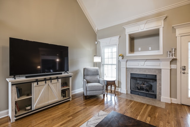 living area featuring a tiled fireplace, crown molding, baseboards, and wood finished floors