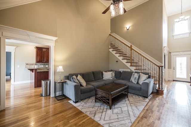 living room with a towering ceiling, light wood finished floors, stairs, and crown molding