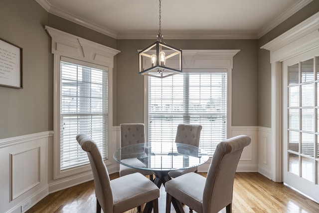 dining room with light wood-style floors, crown molding, and wainscoting