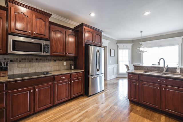 kitchen featuring a sink, ornamental molding, appliances with stainless steel finishes, dark stone counters, and light wood finished floors