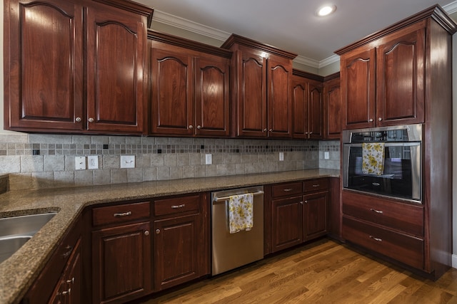 kitchen with light wood-style flooring, ornamental molding, backsplash, stainless steel appliances, and a sink