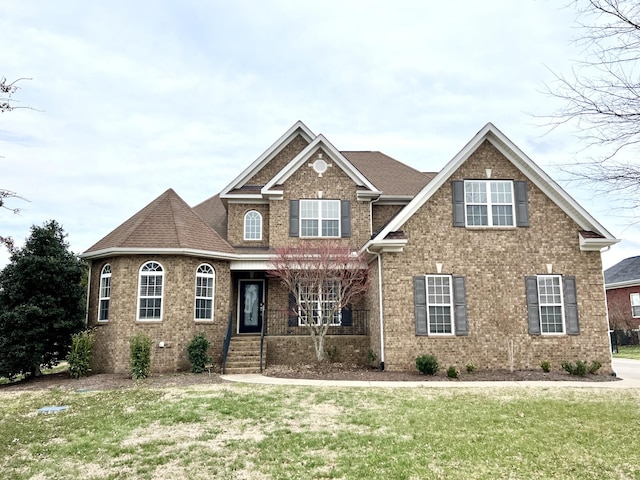 craftsman-style house featuring covered porch, brick siding, a front lawn, and roof with shingles