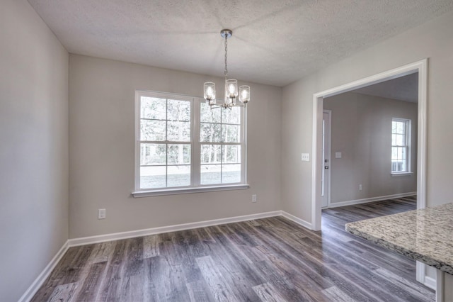 unfurnished dining area with dark wood-type flooring, a chandelier, and a textured ceiling