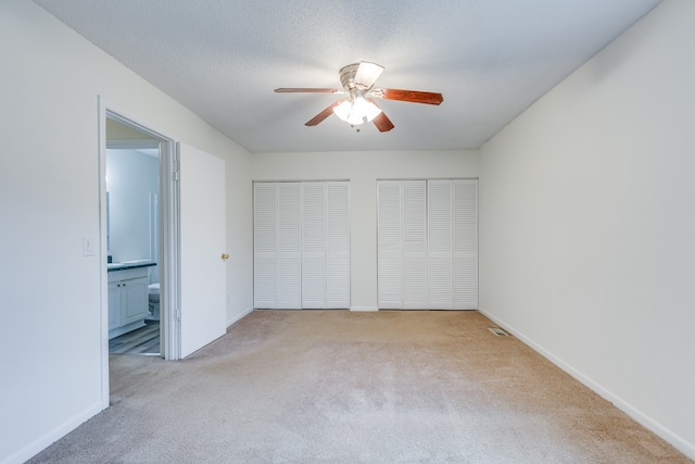 unfurnished bedroom featuring connected bathroom, multiple closets, light carpet, a textured ceiling, and ceiling fan