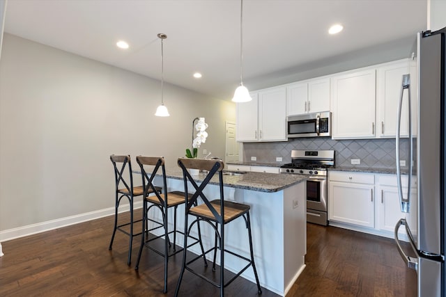 kitchen featuring a kitchen island with sink, stainless steel appliances, a kitchen bar, pendant lighting, and dark hardwood / wood-style flooring