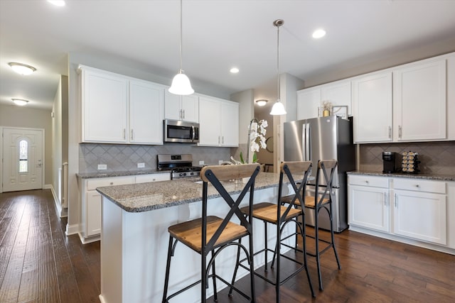 kitchen featuring white cabinets, hanging light fixtures, appliances with stainless steel finishes, dark wood-type flooring, and a center island