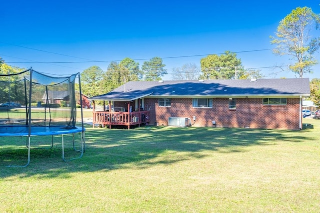 rear view of house with a yard, a trampoline, a deck, and central air condition unit