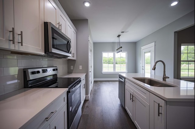 kitchen featuring appliances with stainless steel finishes, sink, an island with sink, white cabinets, and dark wood-type flooring