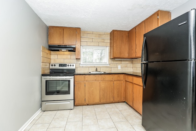 kitchen with stainless steel electric range, light tile patterned floors, backsplash, black fridge, and sink