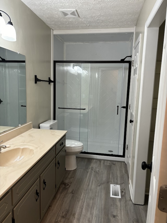 bathroom with a shower with door, a textured ceiling, hardwood / wood-style flooring, toilet, and vanity