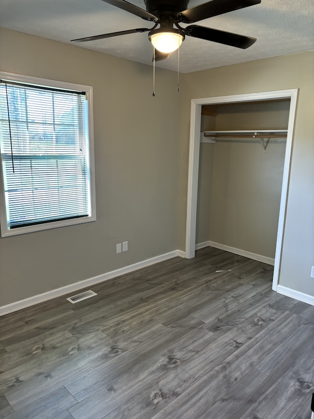 unfurnished bedroom featuring dark wood-type flooring, a textured ceiling, a closet, and ceiling fan