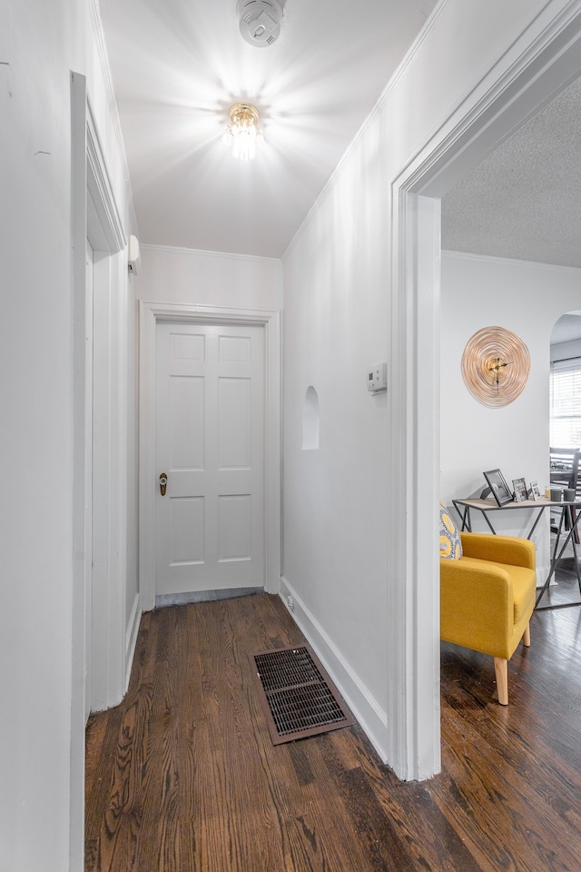 corridor with ornamental molding, dark wood-type flooring, and a textured ceiling