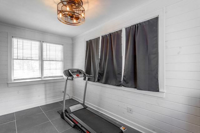 workout room featuring a notable chandelier, dark tile patterned floors, crown molding, and wooden walls