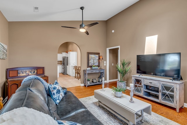 living room with ceiling fan, high vaulted ceiling, and light hardwood / wood-style flooring