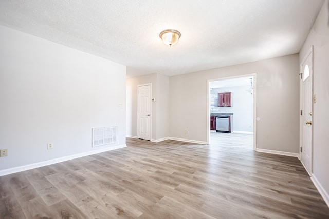 unfurnished room with a textured ceiling and light hardwood / wood-style floors