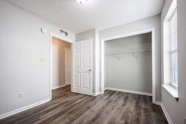 unfurnished bedroom featuring dark wood-type flooring, a closet, a textured ceiling, and multiple windows