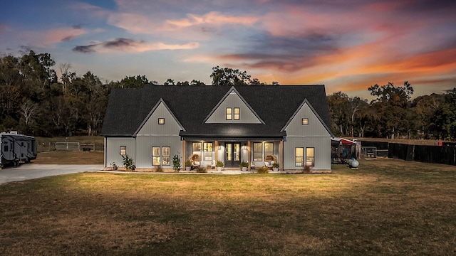 back house at dusk with covered porch and a lawn