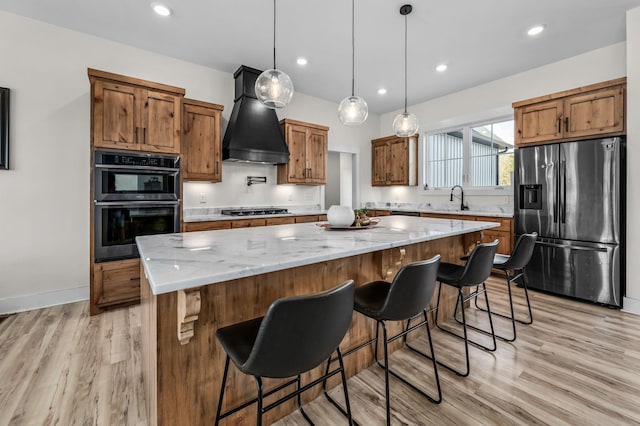 kitchen featuring appliances with stainless steel finishes, light wood-type flooring, a large island, decorative light fixtures, and premium range hood