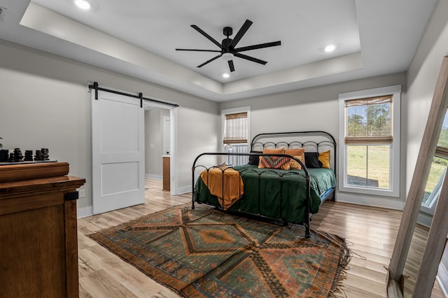 bedroom with wood finished floors, baseboards, a tray ceiling, recessed lighting, and a barn door