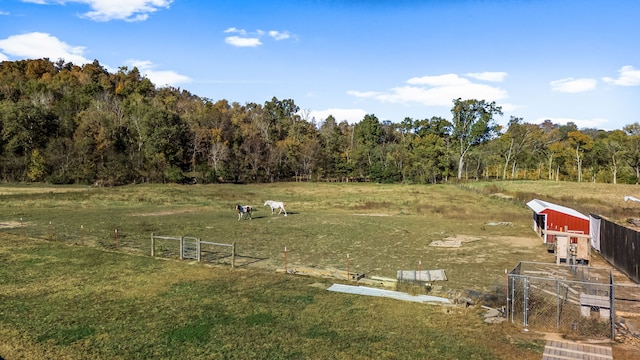 view of yard featuring a rural view, a wooded view, and fence