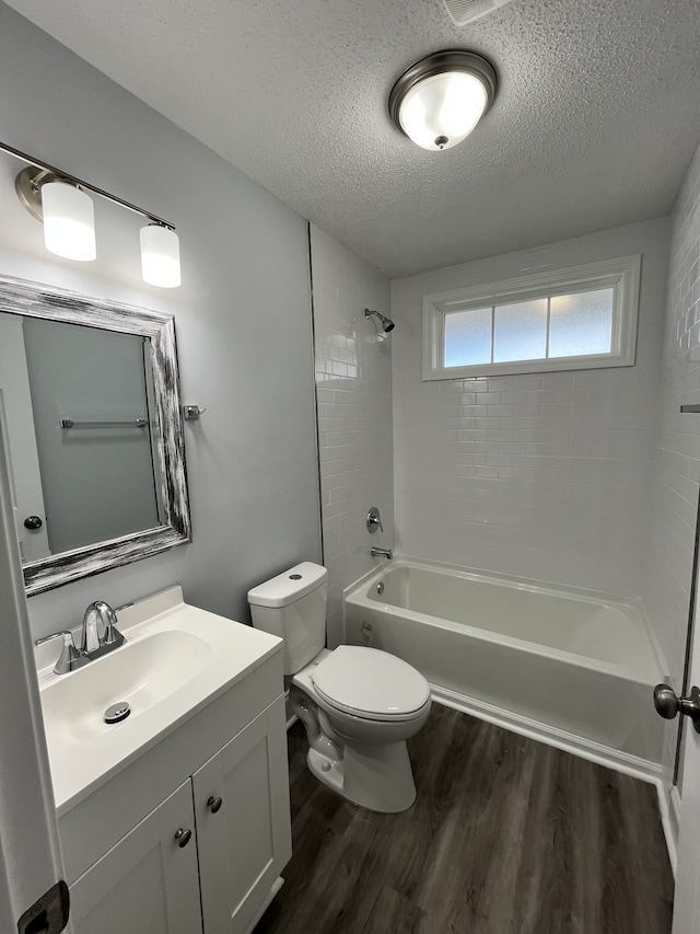 full bathroom featuring tiled shower / bath, a textured ceiling, hardwood / wood-style flooring, toilet, and vanity