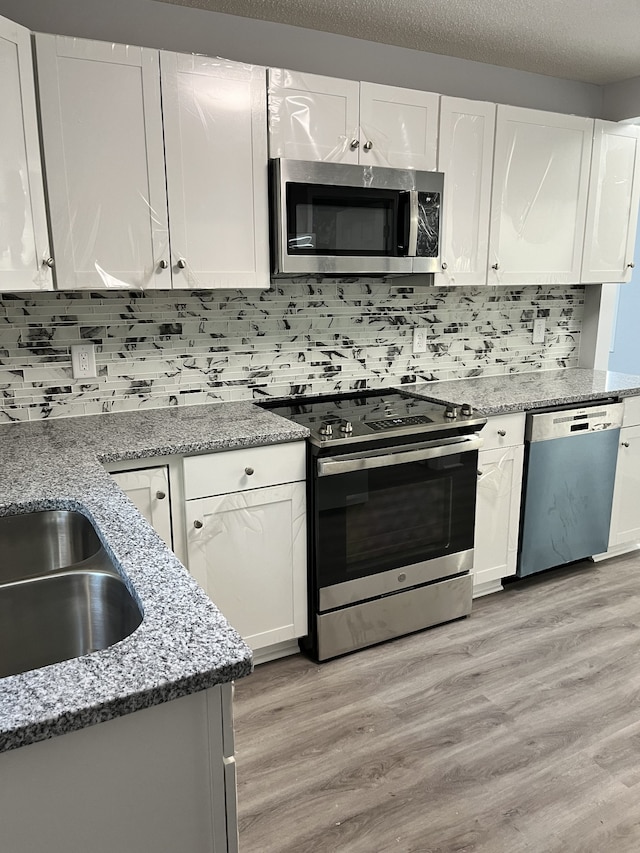 kitchen featuring decorative backsplash, stainless steel appliances, light stone countertops, light wood-type flooring, and white cabinetry