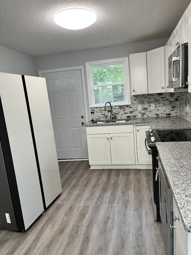 kitchen with white cabinets, backsplash, light hardwood / wood-style flooring, sink, and stainless steel appliances