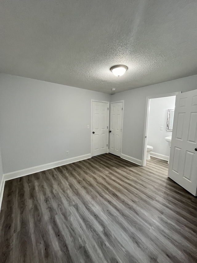 unfurnished bedroom featuring dark wood-type flooring, ensuite bath, and a textured ceiling