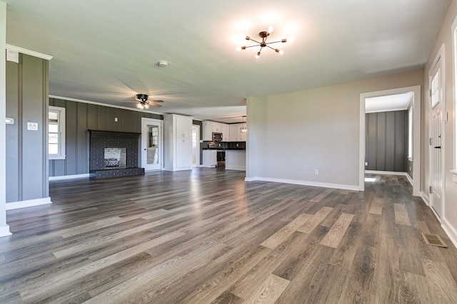 unfurnished living room with ornamental molding, dark wood-type flooring, and ceiling fan with notable chandelier